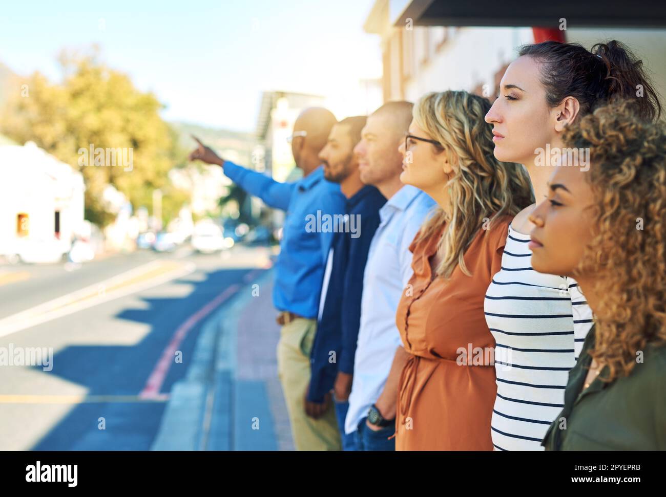 All lined up in a row. a group friends standing and looking into the distance next to a street outside. Stock Photo