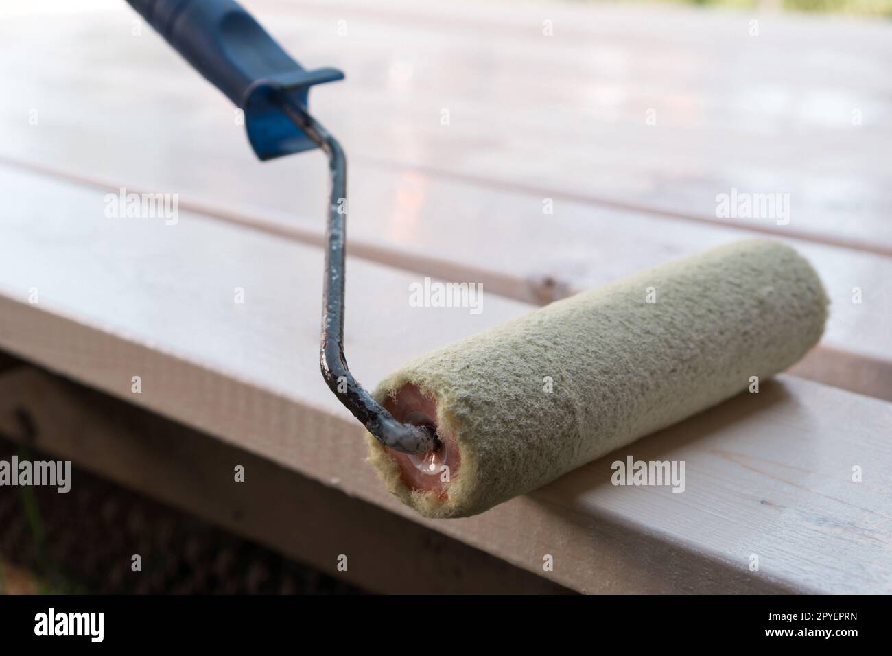 Close up white soft professional paint roller applicator with handle lying on wooden board. Making cosmetic repairment Stock Photo