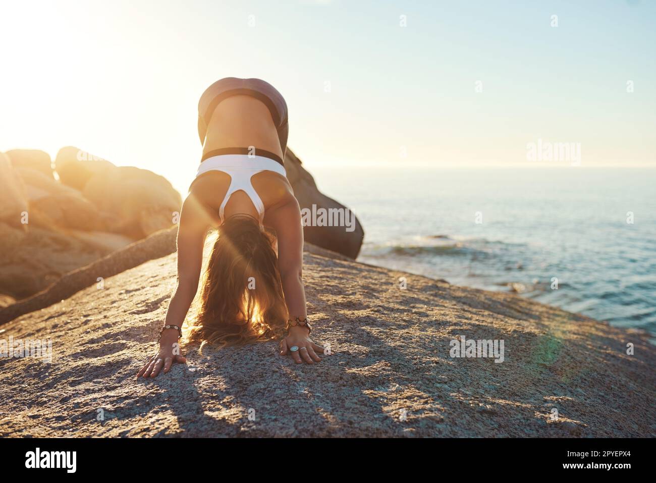 Because yoga will get you back on track. an athletic young woman practicing yoga on the beach. Stock Photo