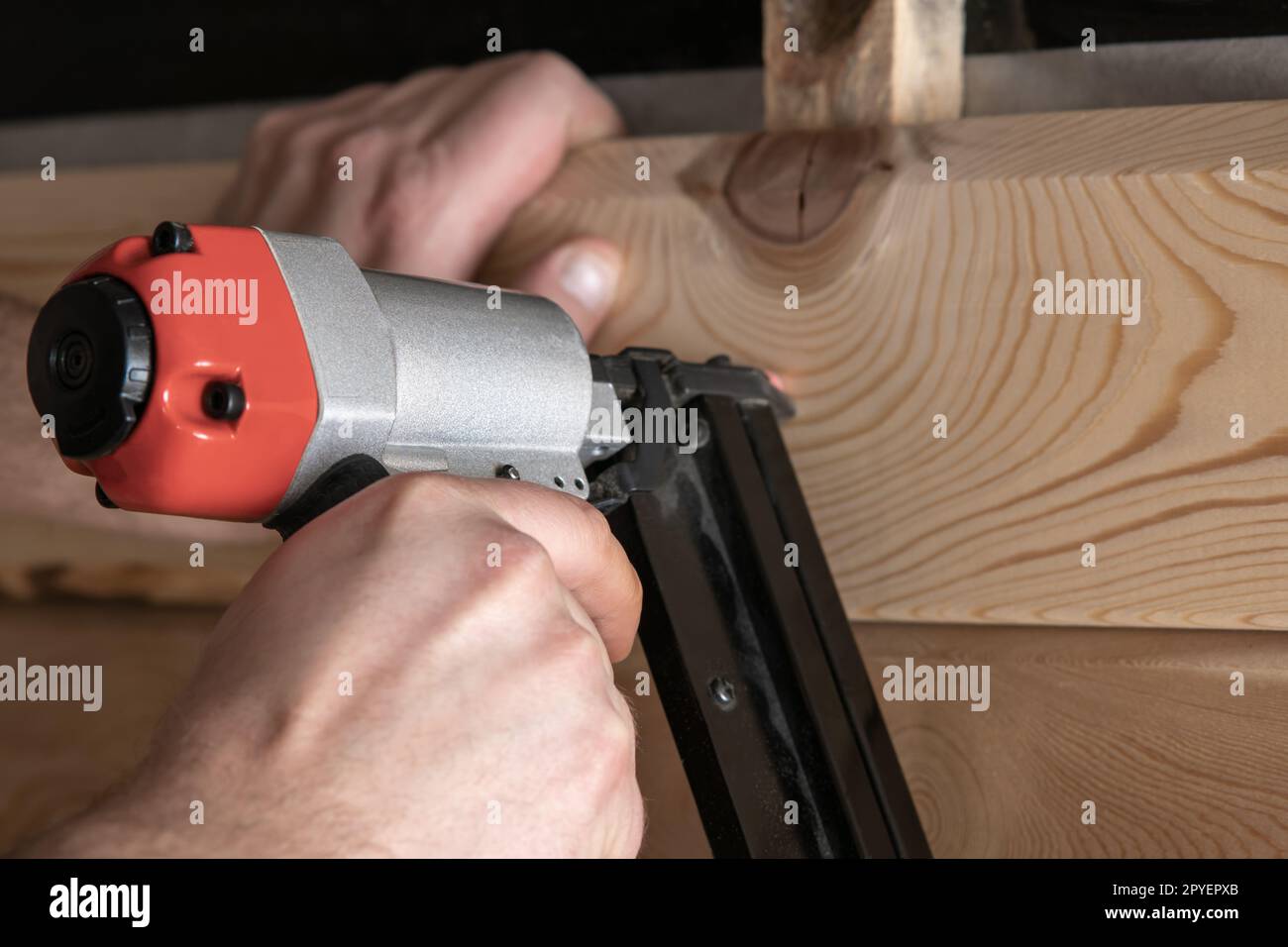 Close up cropped carpenter male hands use pneumatic nailer, stapler gun for wood timber plank. Craftsmanship, handcraft Stock Photo