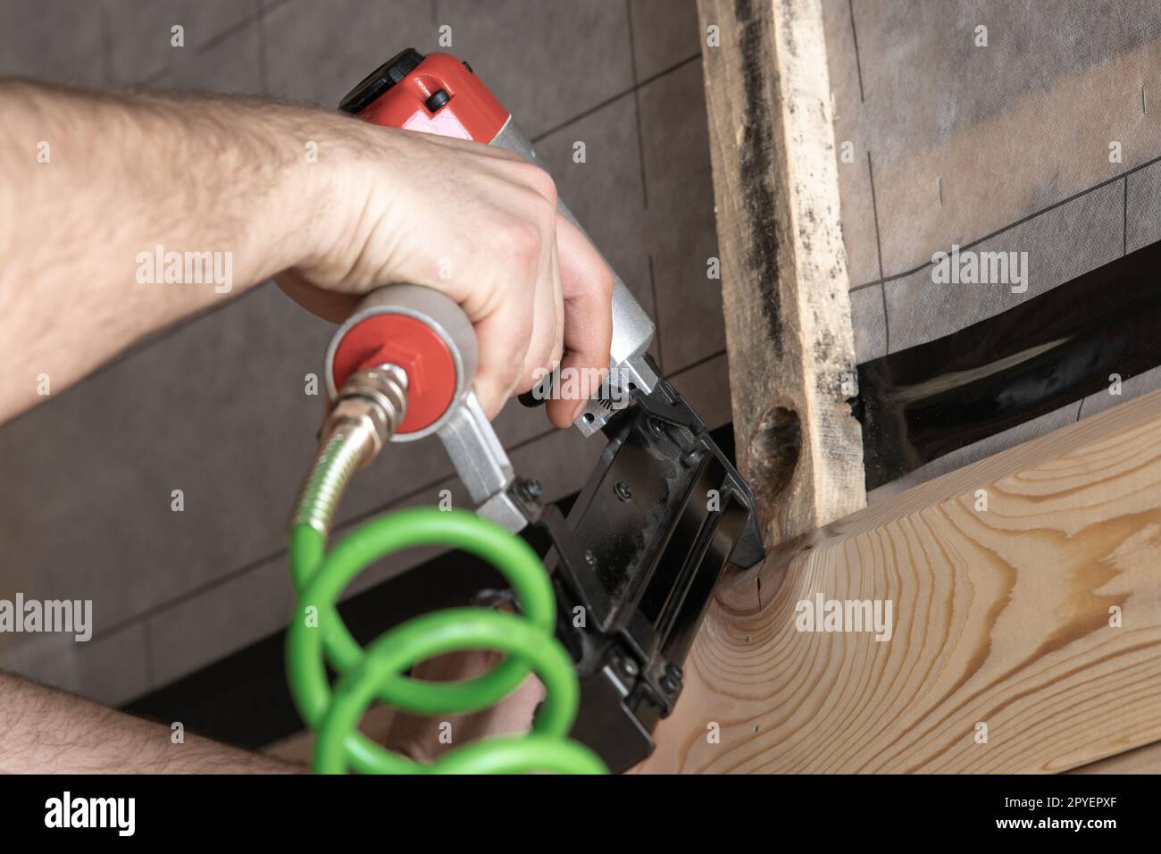 Cropped man hands working with stapler, nail gun with green cable and wooden board. Craft carpenter and builder work Stock Photo