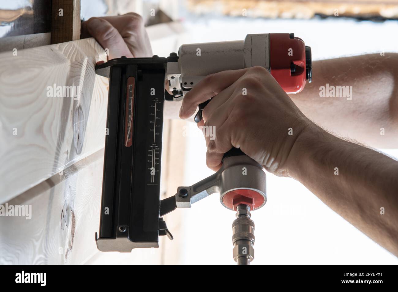 Cropped male builder hands use pneumatic stapler gun for clipping wooden timber board. Scoring metal nails and staples Stock Photo