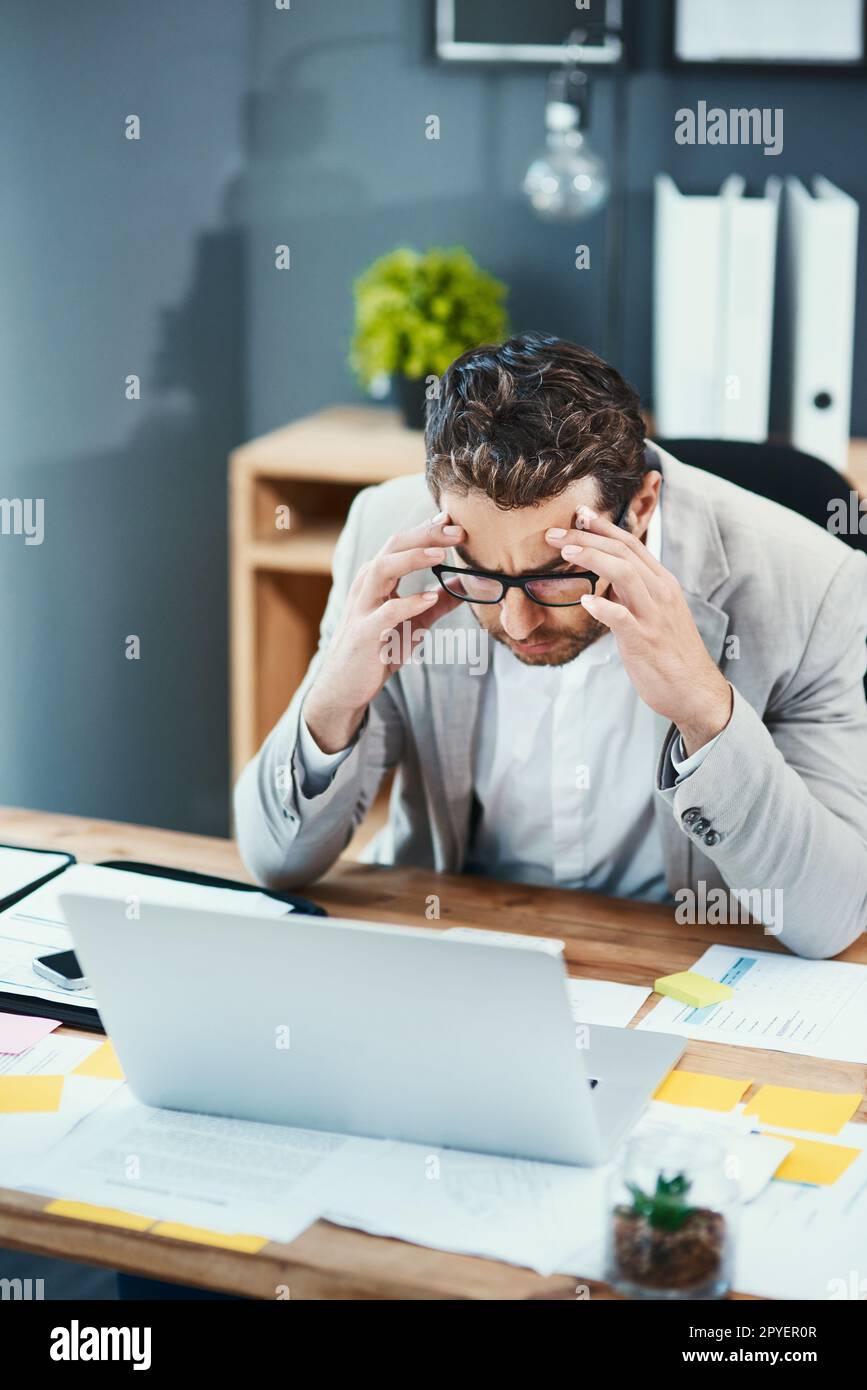 Tension headaches can put a damper on your day. a young businessman looking stressed out while working on a laptop in an office. Stock Photo