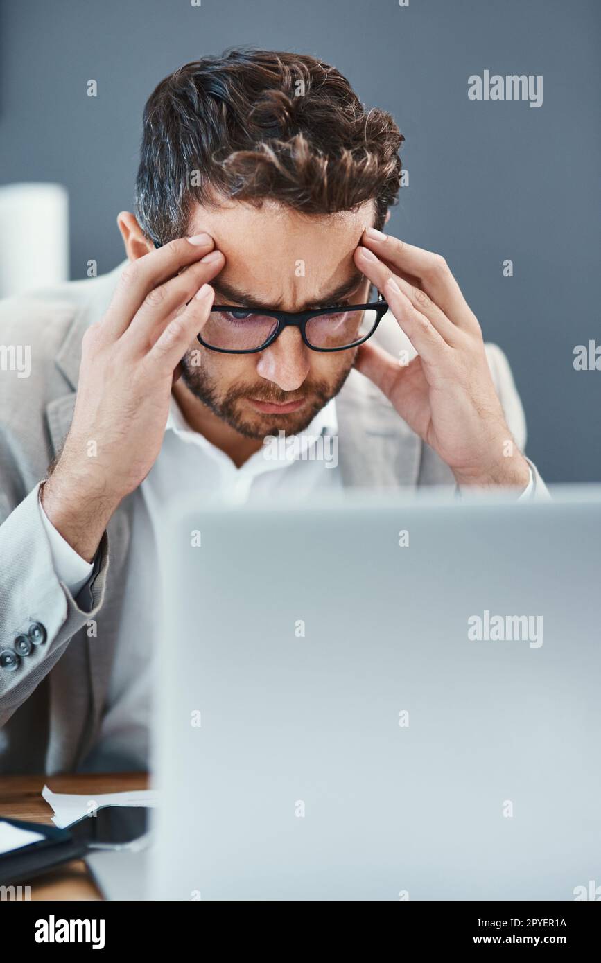 Headaches hamper your productivity. a young businessman looking stressed out while working on a laptop in an office. Stock Photo