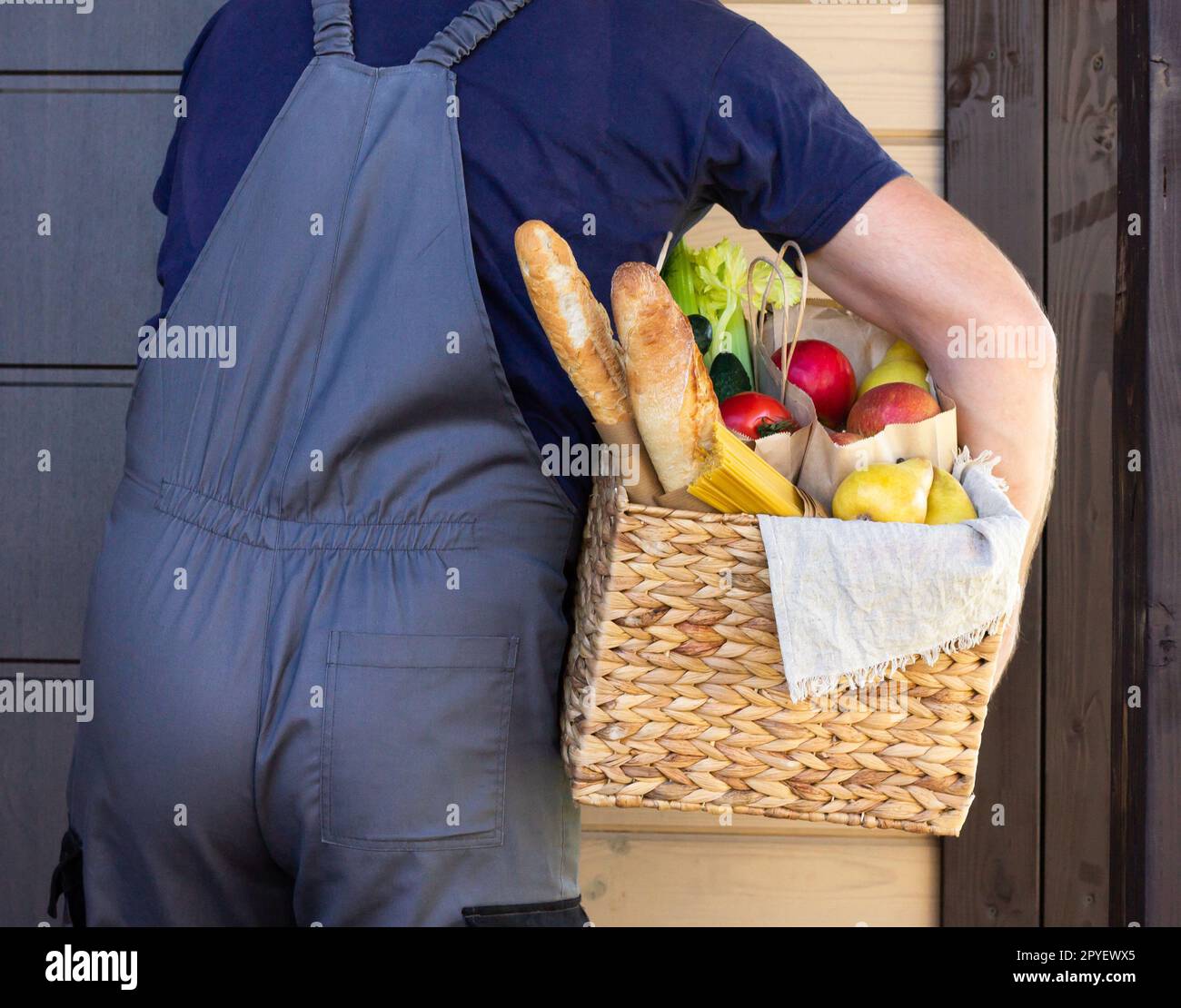 Fresh organic food in a wicker basket in the hands of a bicycle courier. Bike delivery or donation of food concept. Stock Photo