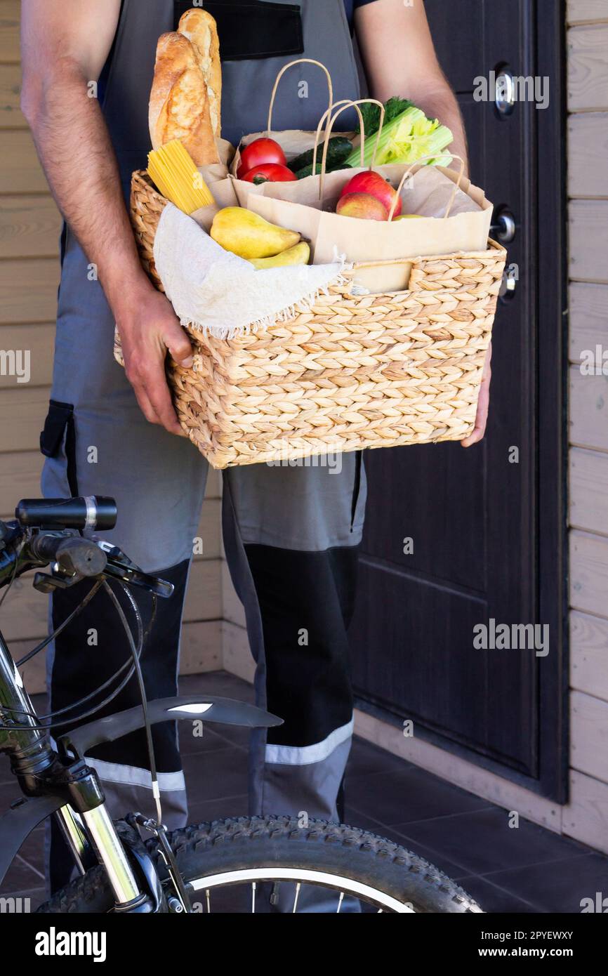 Fresh organic food in a wicker basket in the hands of a bicycle courier. Bike delivery or donation of food concept. Stock Photo
