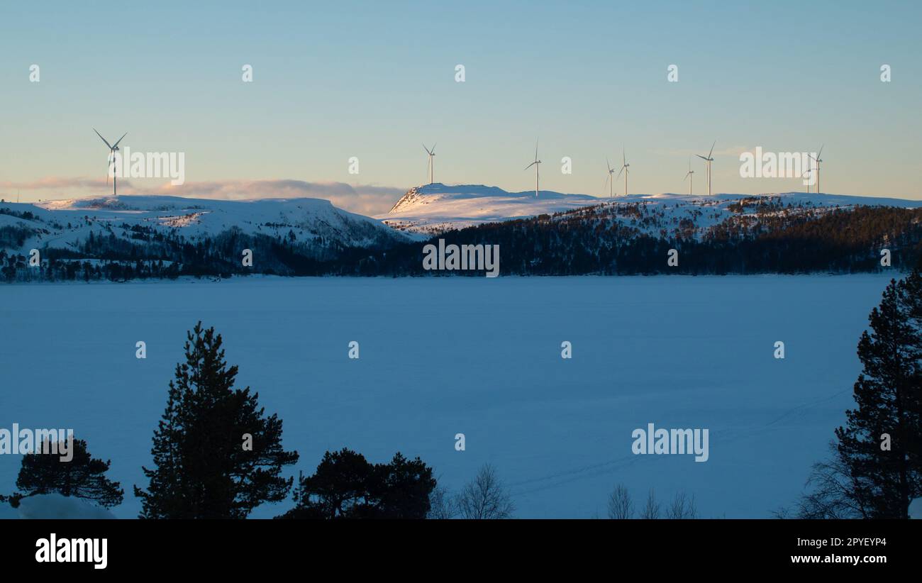 Lot of wind turbines on a snow-capped mountain in the evening at sunset Stock Photo