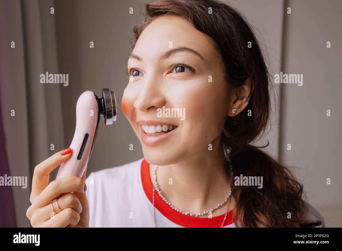 Girl using face massage device that is equipped with laser, vibration