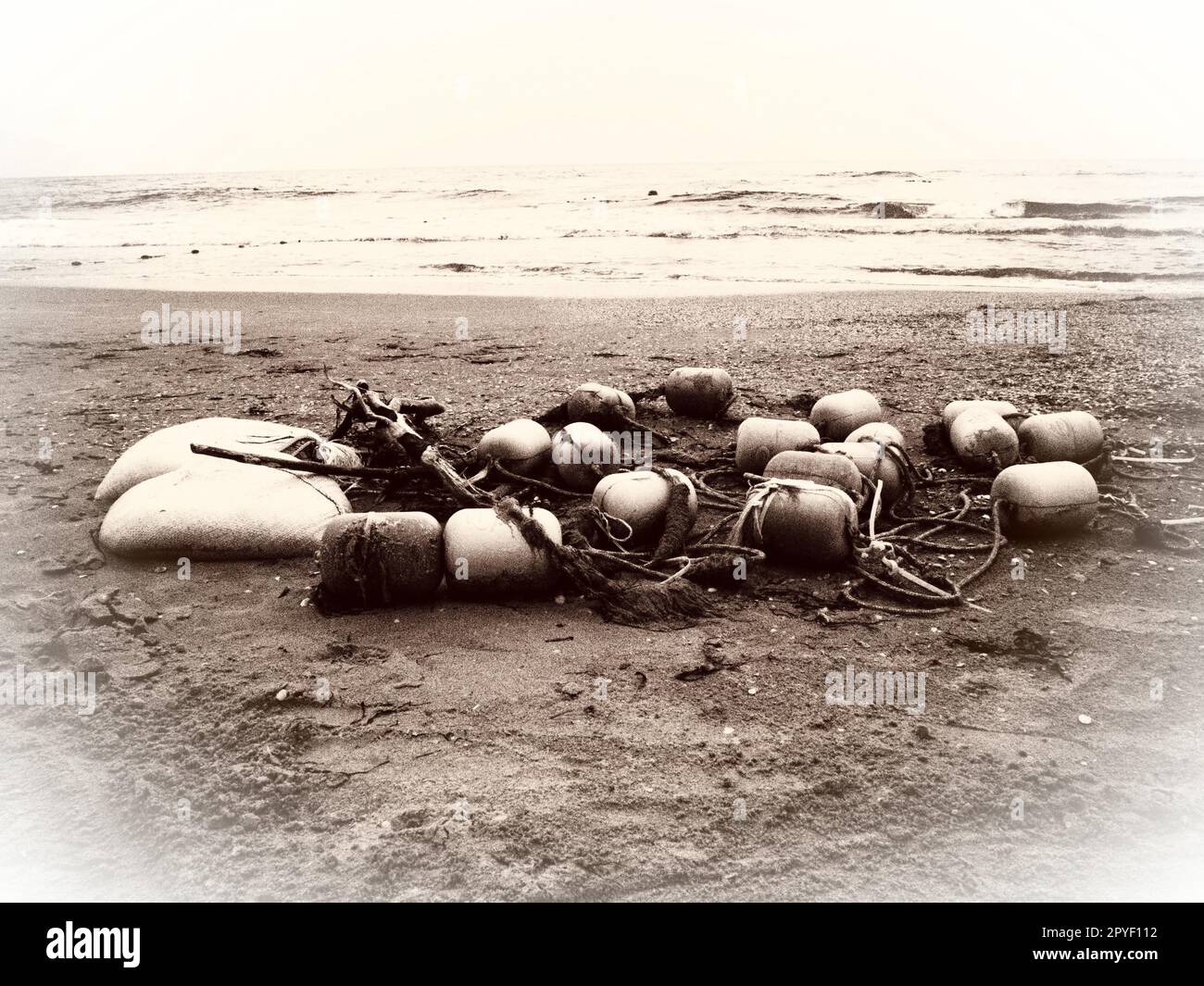 Buoys in the sand. A beach with wet coarse quartz sand. Tangled ropes and plastic buoys left on the shore. Safety equipment. The end of the summer season. Stormy weather at sea or ocean. Low tide. Stock Photo