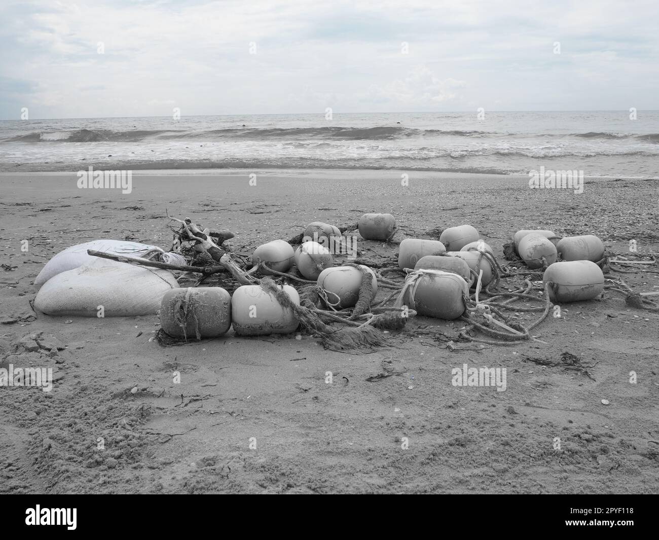 Buoys in the sand. A beach with wet coarse quartz sand. Tangled ropes and plastic buoys left on the shore. Safety equipment. The end of the summer season. Stormy weather at sea or ocean. Low tide. Stock Photo