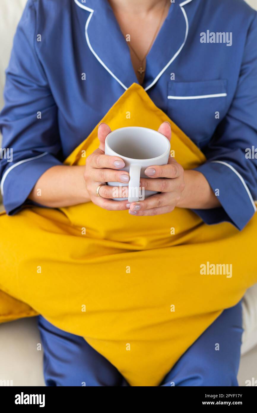 Close-up woman in cozy pajamas resting on sofa at home and drinks tea or coffee - wellbeing and comfort morning concept Stock Photo