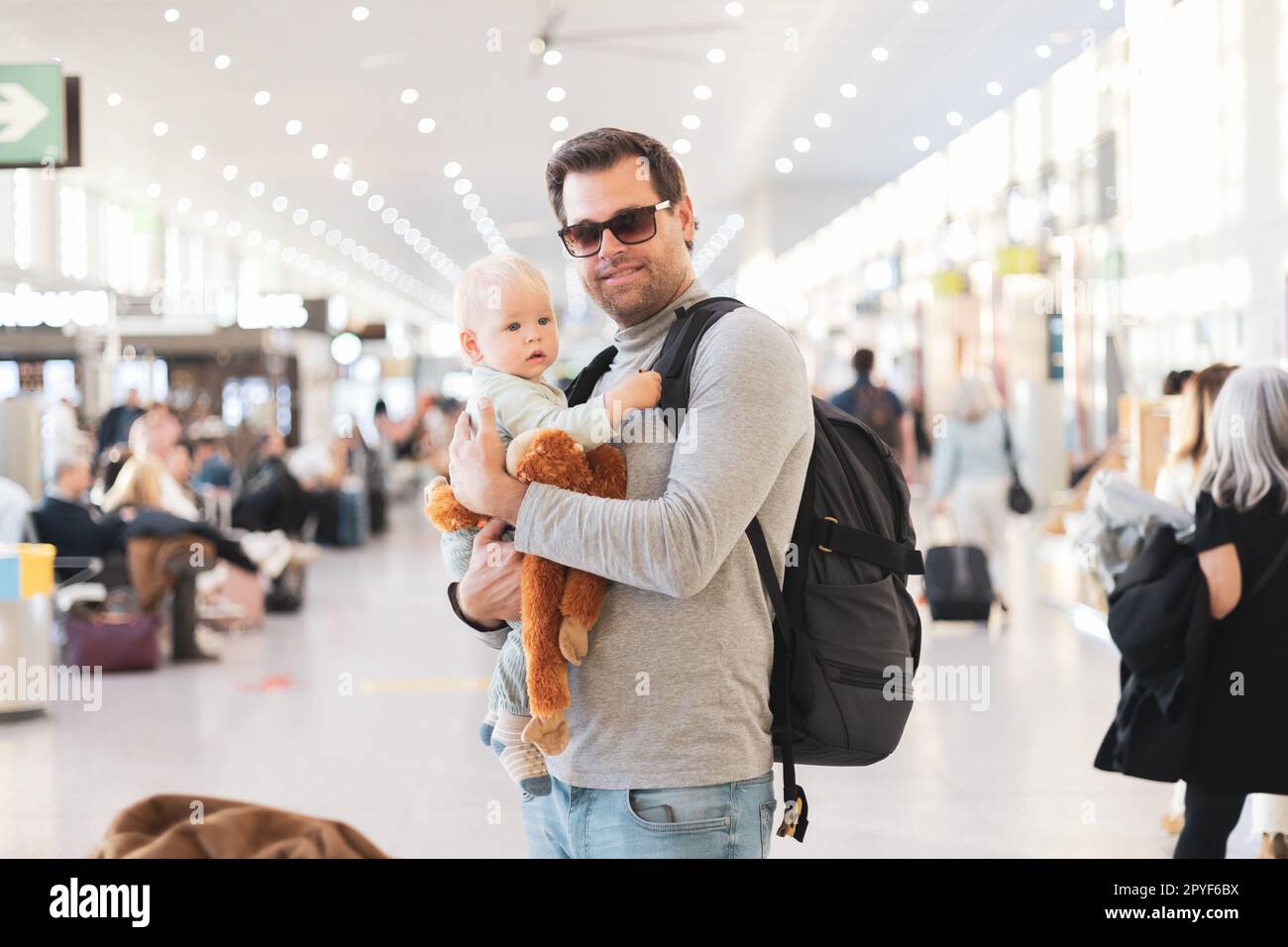 Father traveling with child, holding his infant baby boy at airport terminal waiting to board a plane. Travel with kids concept. Stock Photo