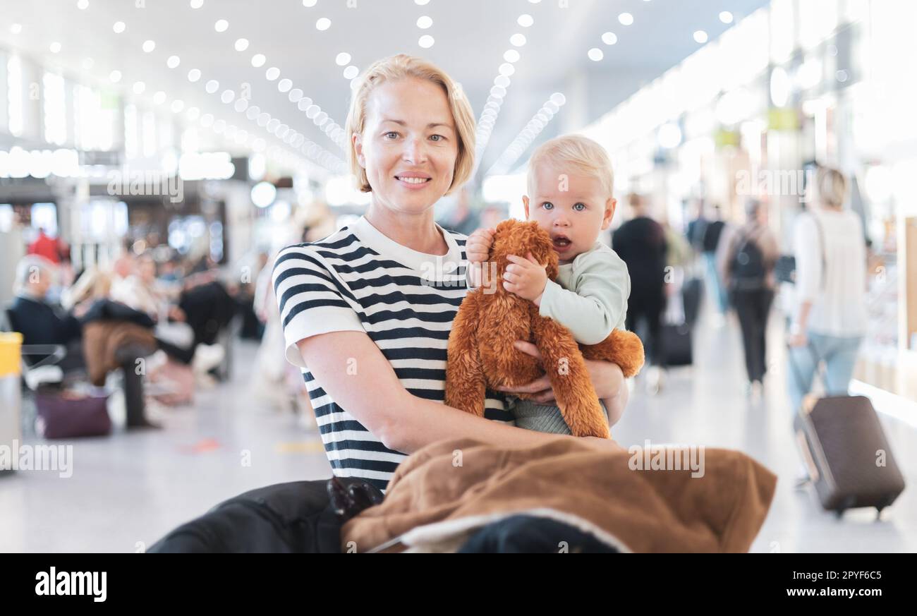 Mother traveling with child, holding his infant baby boy at airport terminal waiting to board a plane. Travel with kids concept. Stock Photo