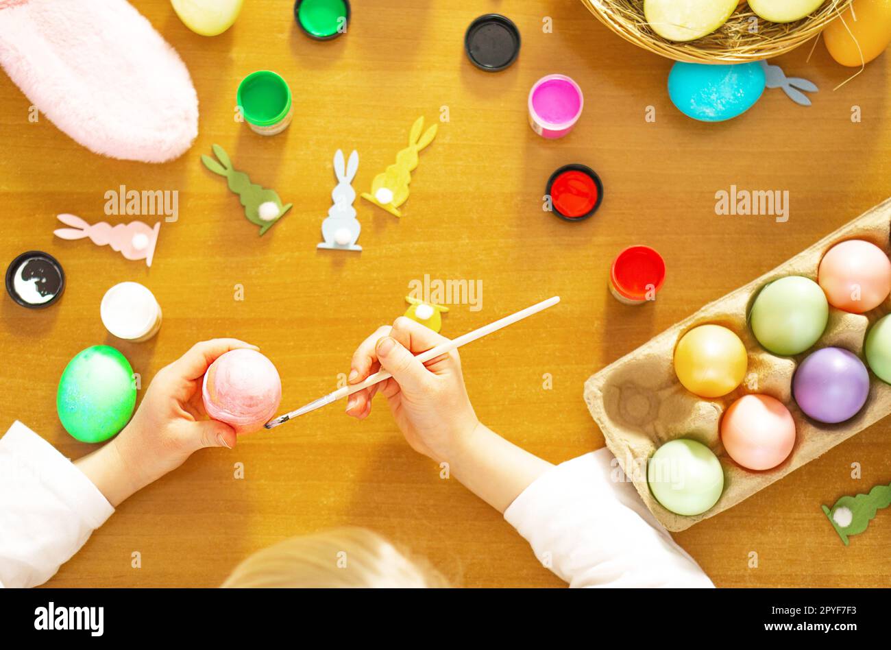 Child hands painting eggs for Easter on the wooden table at home. Preparation for Easter. Stock Photo