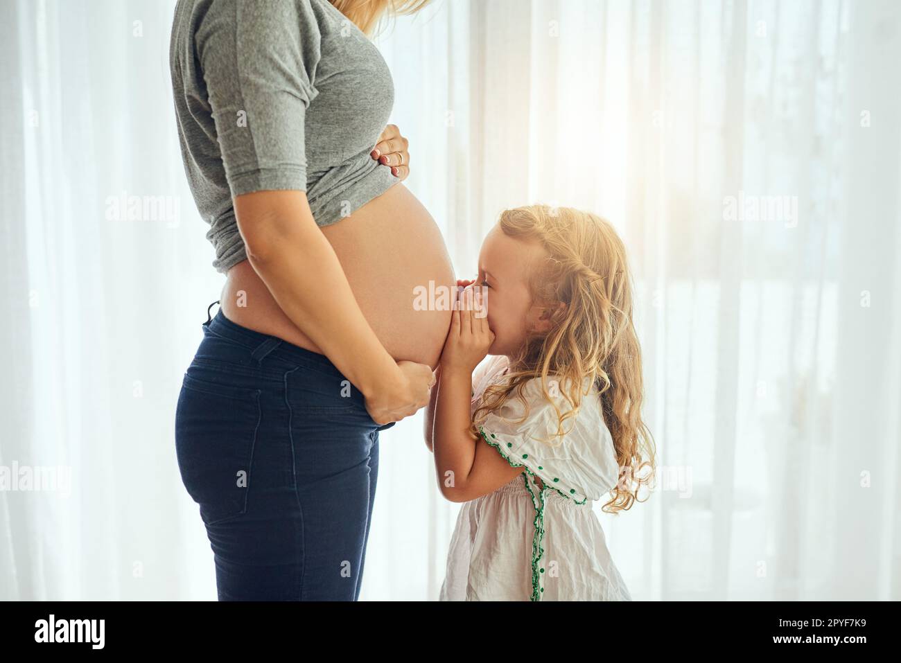 Its clear that theyll have a close bond. a little girl whispering to her mothers pregnant belly. Stock Photo