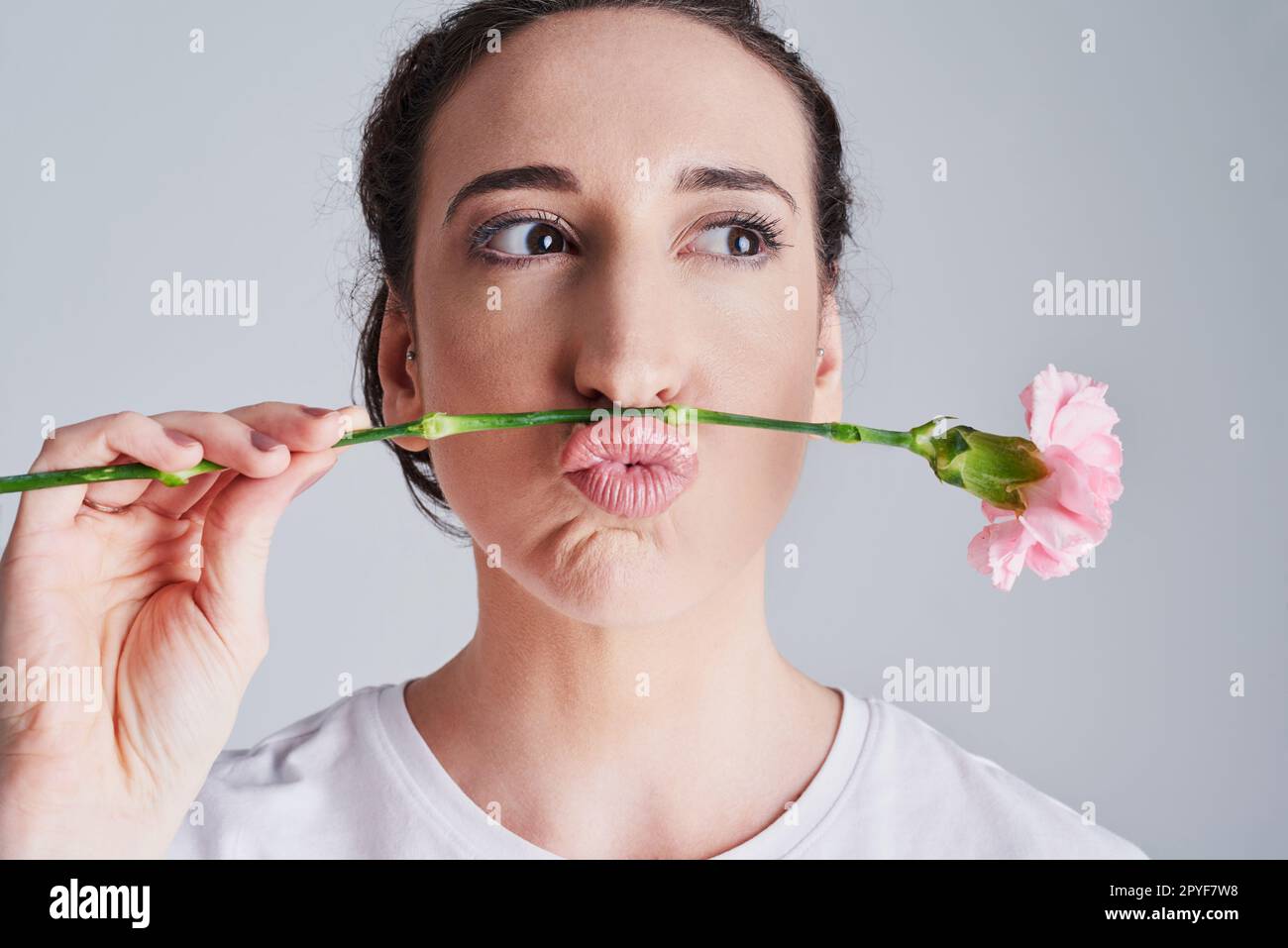 This is called a womans moustache. Studio shot of a beautiful young woman making a face with a pink flower against a grey background. Stock Photo