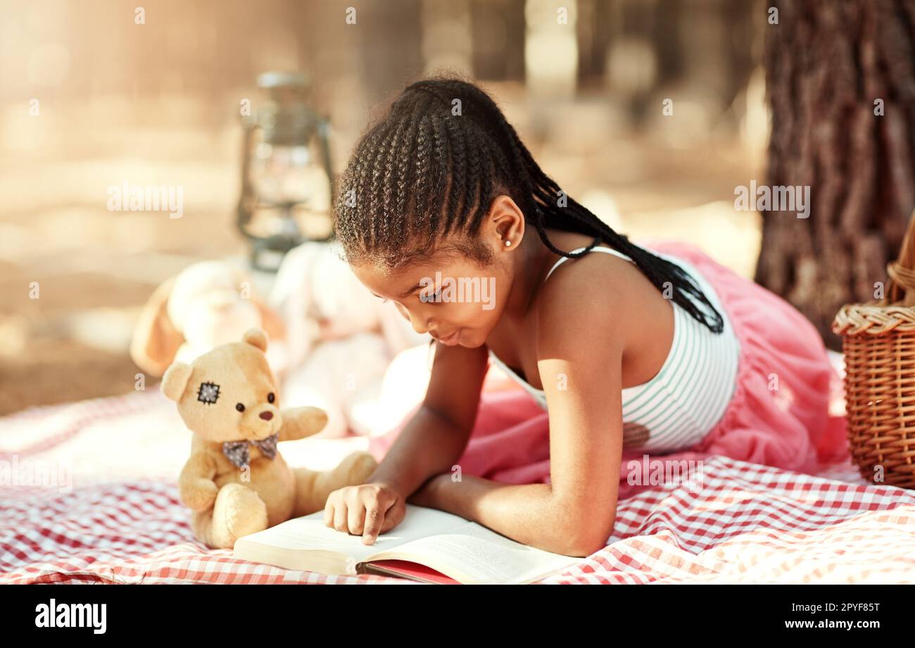 Shes slowly starting to become a keen reader. a little girl reading a book with her toys in the woods. Stock Photo
