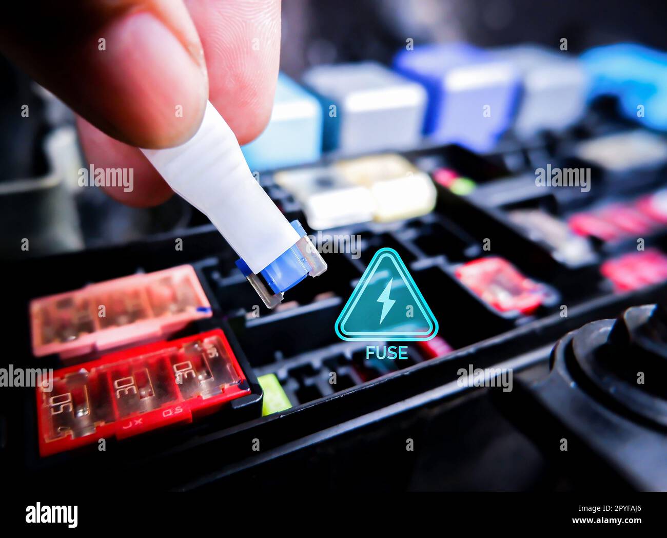 Close up of mini fuse for electric car system with a voltage caution symbol and fuse box on blurred background, automotive parts concept. Stock Photo