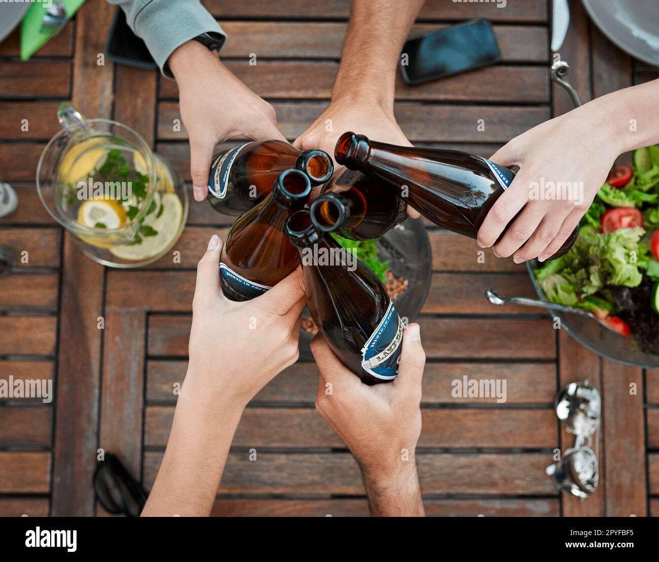 Heres to us. High angle shot of a group unrecognizable peoples hands holding beer bottles and toasting outside around a table. Stock Photo