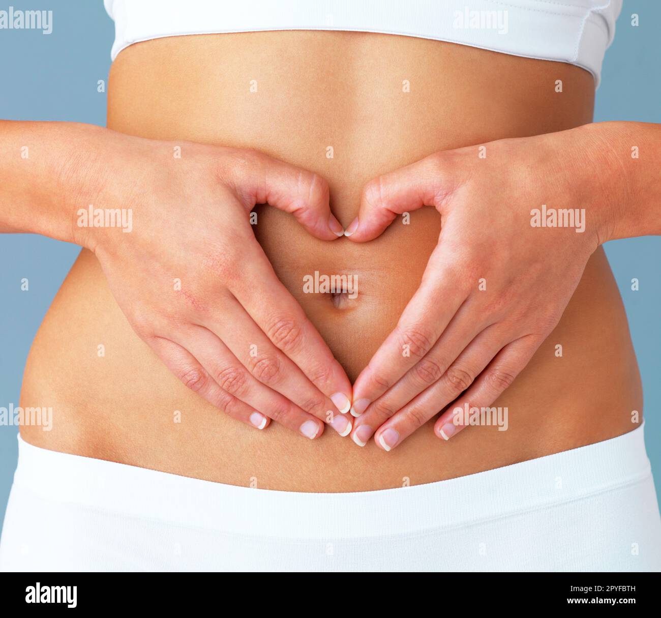 Healthy starts with the stomach. Cropped studio shot of a fit young woman making a heart shaped gesture over her stomach against a blue background. Stock Photo