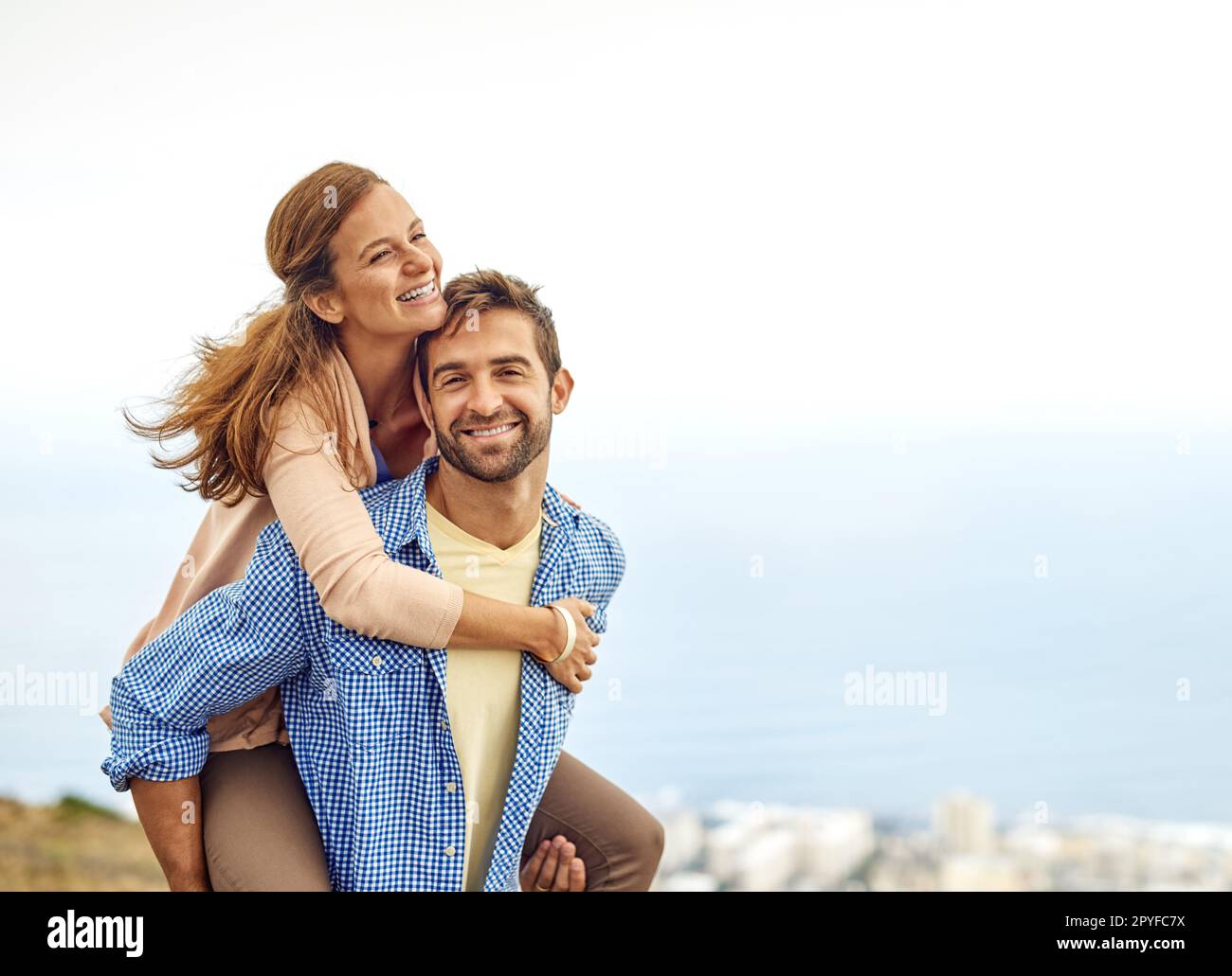 Making the most of a sunny day. a man piggybacking his girlfriend while spending the day outdoors. Stock Photo
