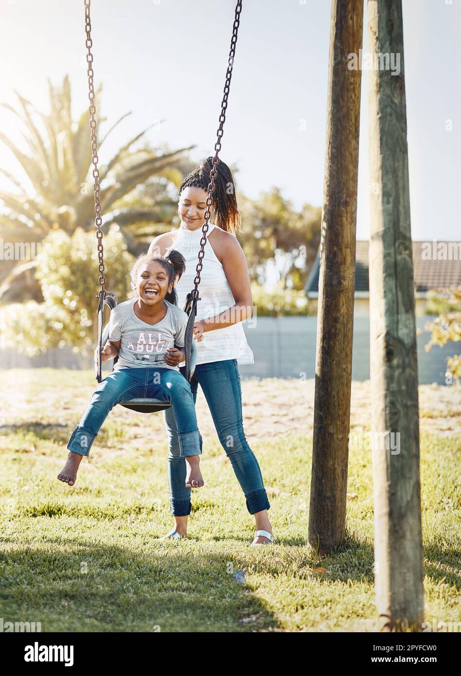 Her laughter brightens the day even more. a mother pushing her daughter on a swing at the park. Stock Photo