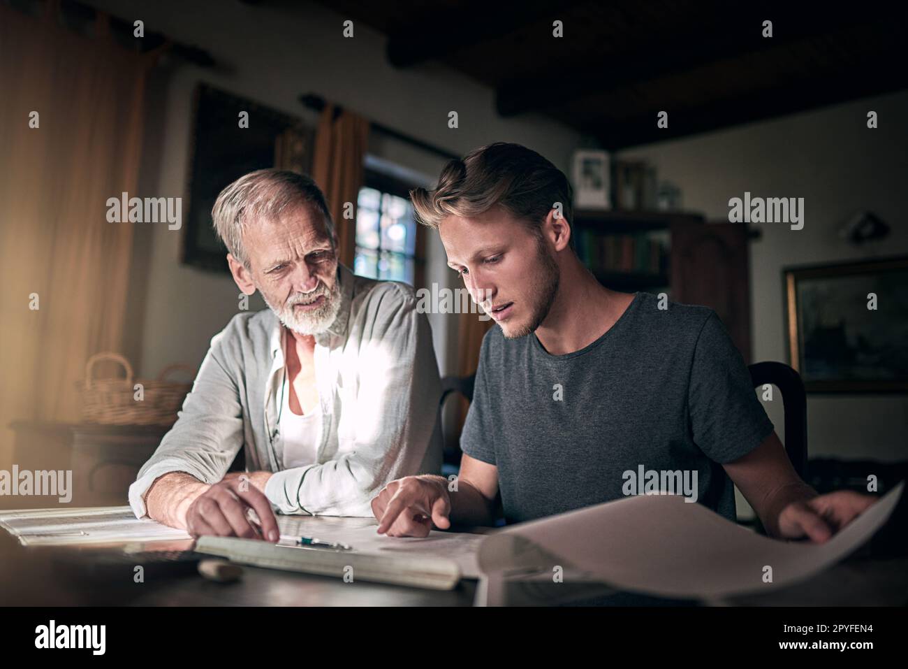 Sometimes it helps to have a fresh set of eyes. a father and his son working on a design for their family business at home. Stock Photo