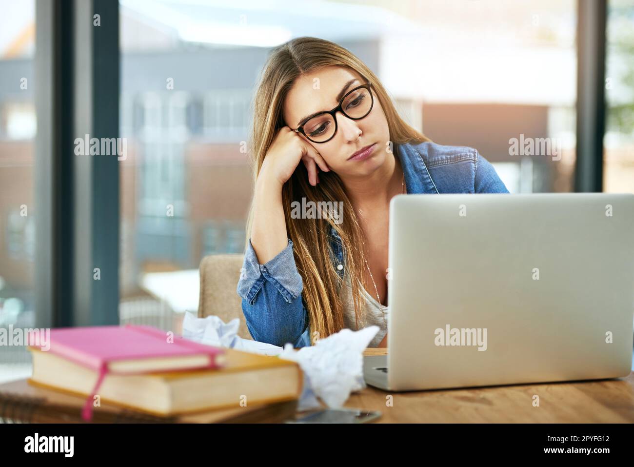 Homework got you down. a female university student looking bored while sitting at a table on campus using a laptop. Stock Photo