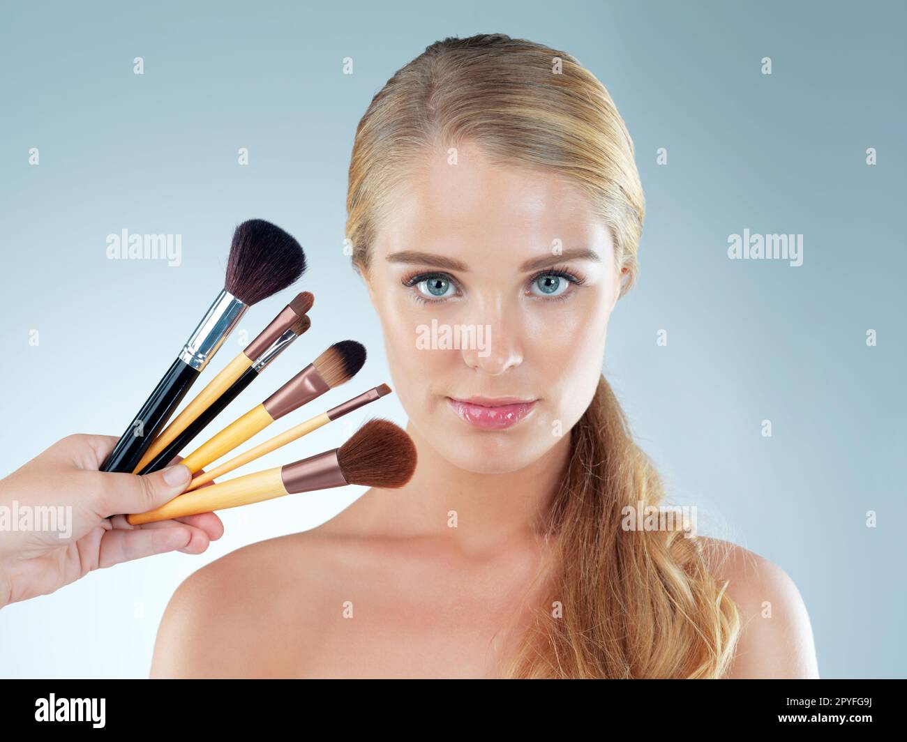Every kind of brush for every kind of makeup. Studio portrait of a beautiful young woman posing with makeup brushes against a blue background. Stock Photo