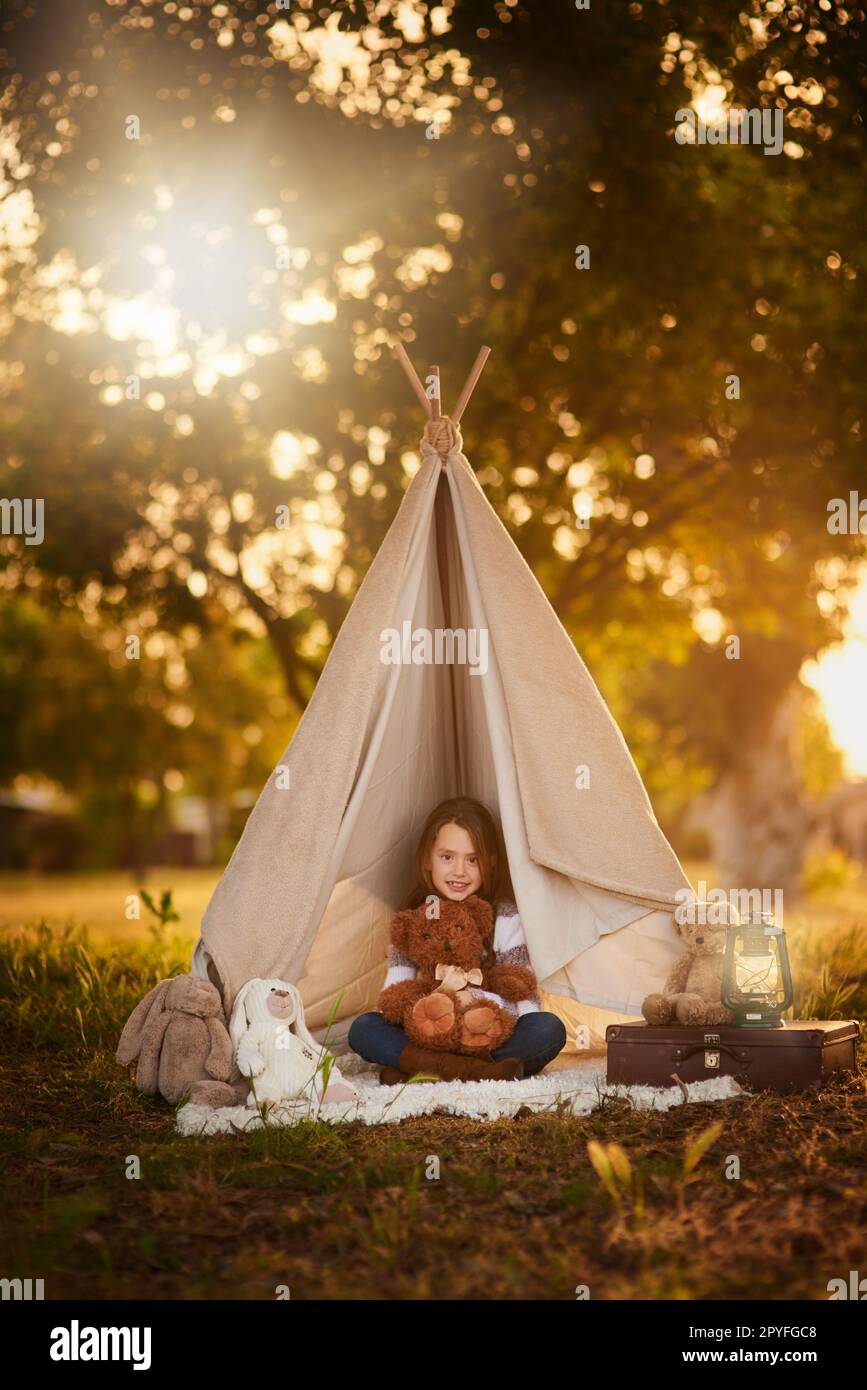 Camping out with Ted. Portrait of a cute little girl playing in her teepee outside. Stock Photo