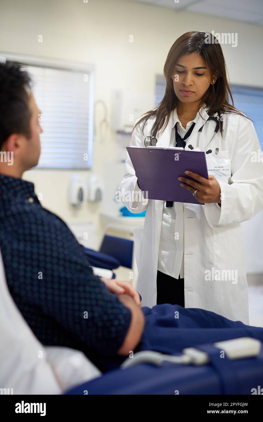 Noting her patients diagnosis. a doctor attending to a patient in a ...