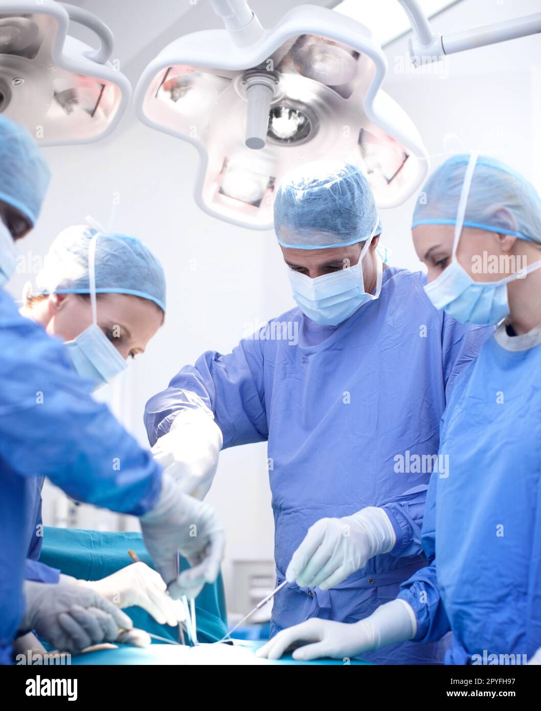 Doctors at work. Diverse group of surgeons working together wearing scrubs in an operating room. Stock Photo