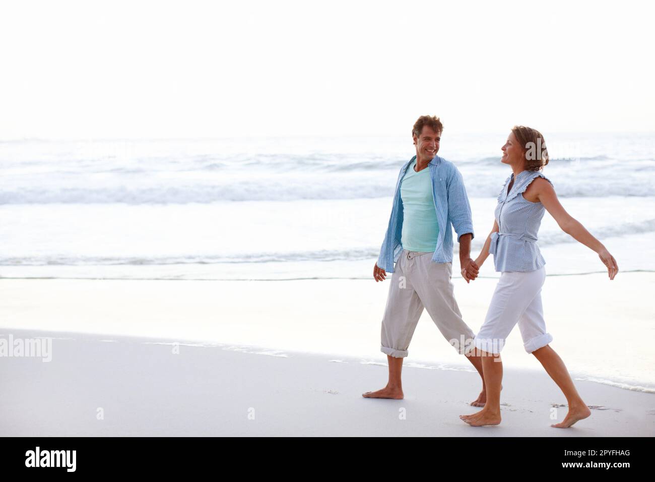 Walking through life together - True Love. A happy couple walking hand in hand on the beach together. Stock Photo