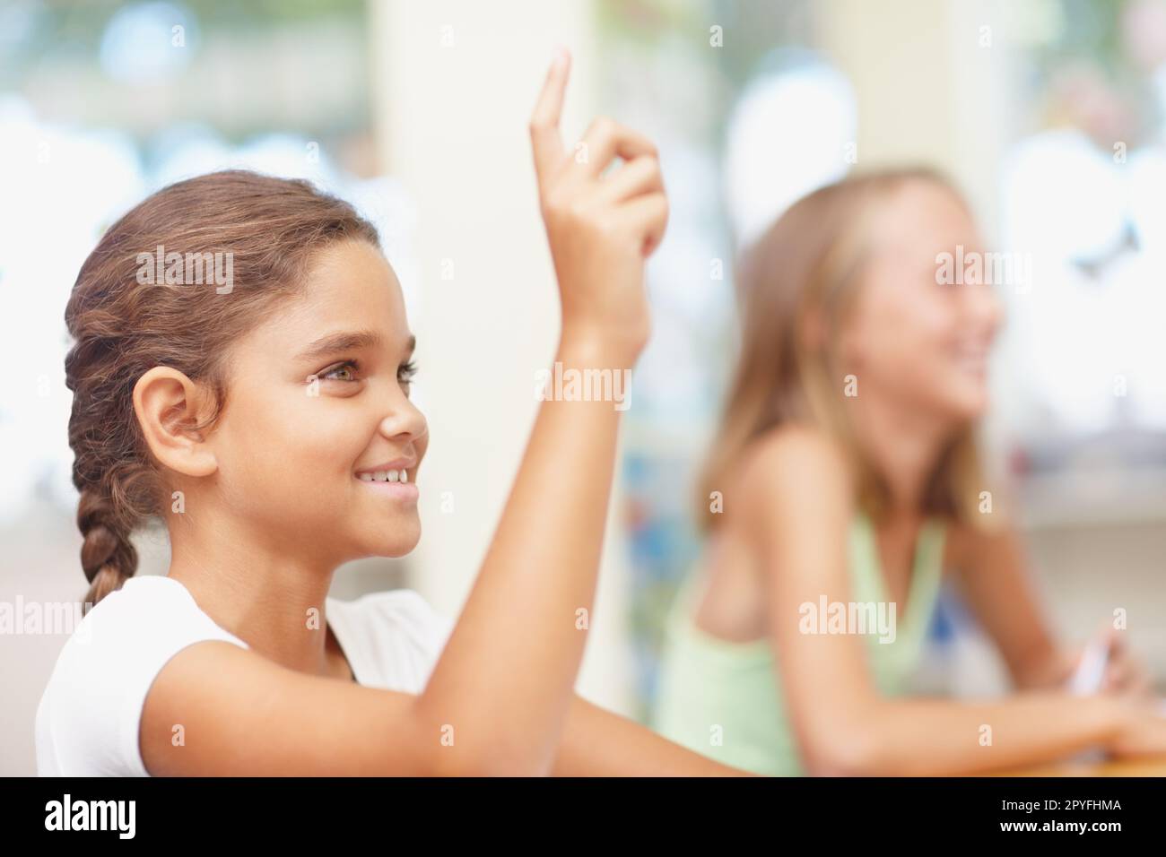 Lets hear what the youth have to say. Pretty young multi-ethnic schoolgirl raising her hand confidently in class - copyspace. Stock Photo