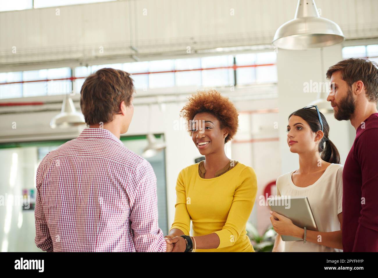 I cant wait to see what you can do. two people shaking hands in an office while their coworkers look on. Stock Photo