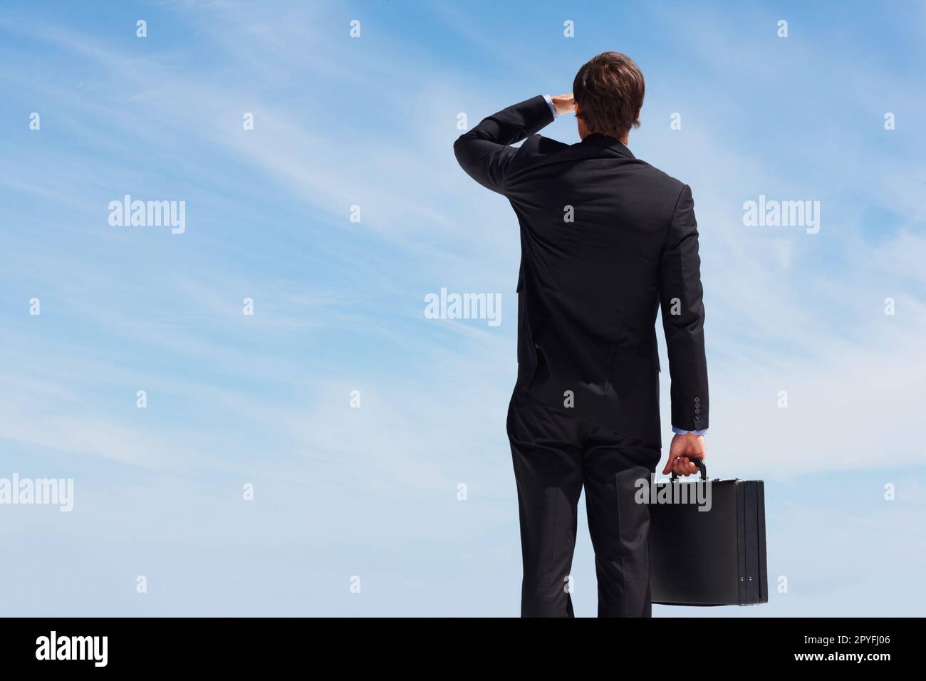 Business man with a briefcase looking at the sky. Rear view of a young business man with a briefcase looking at the blue sky. Stock Photo