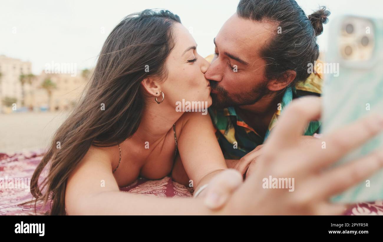 Man and woman kissing and making video call using mobile phone on the beach Stock Photo