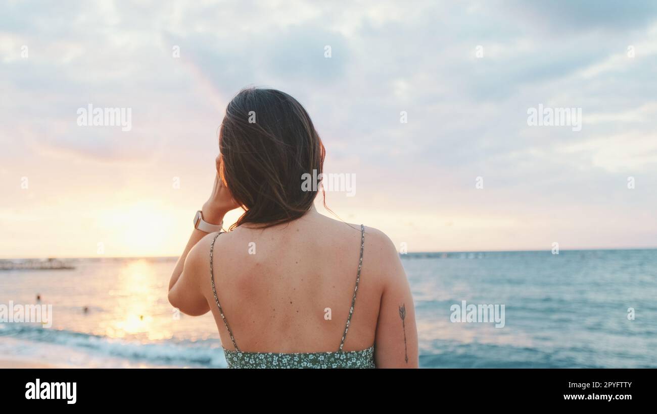 Young woman standing on the beach looking at the sunrise. Back view ...