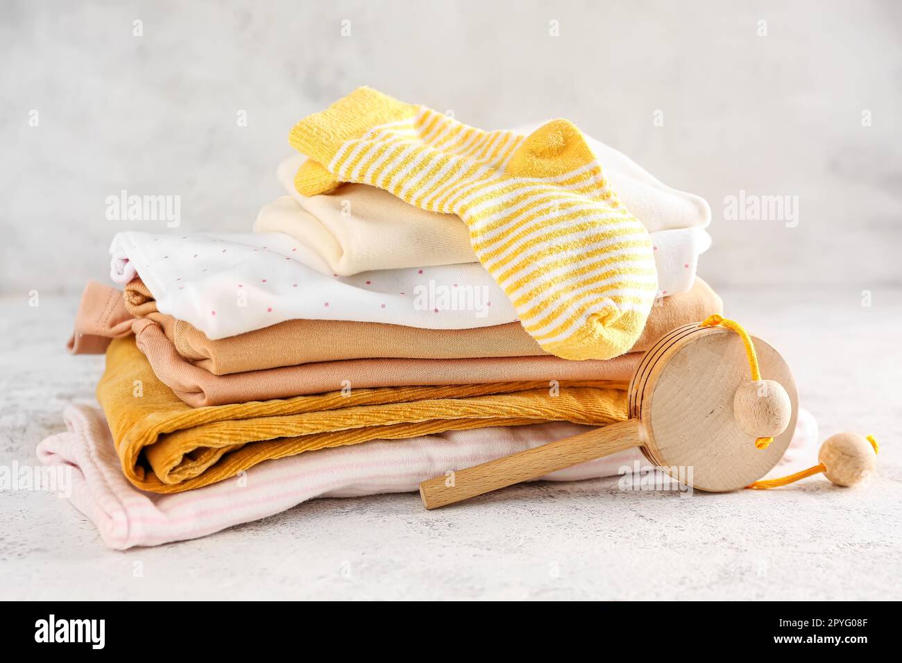 Stack of baby clothes and wooden toy on light background Stock Photo ...