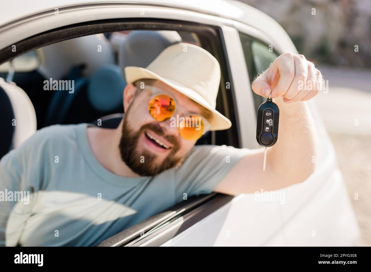Car driver man smiling showing new car keys and car. Bearded guy