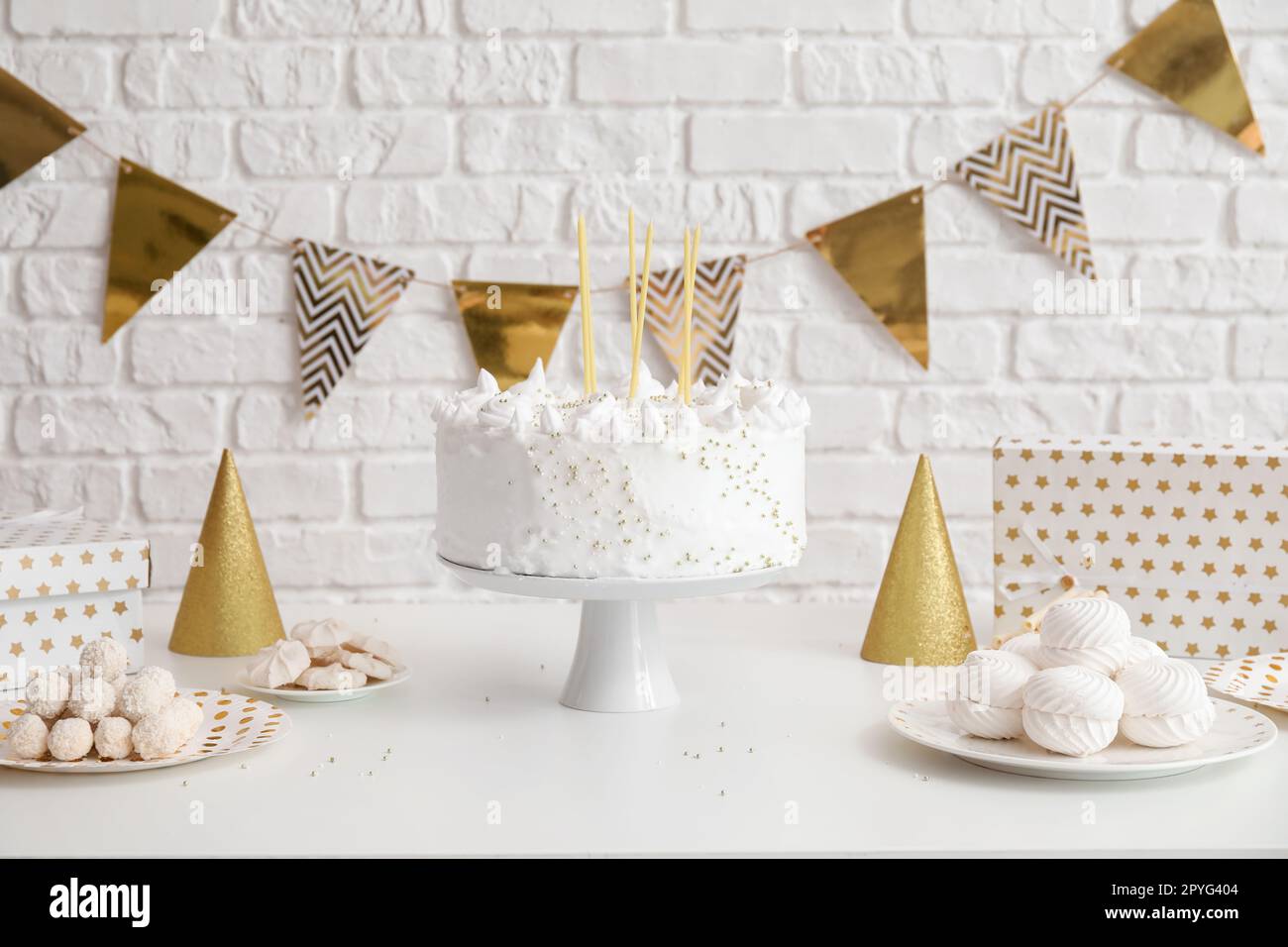 Birthday cake with candles and sweets on white table near brick wall ...