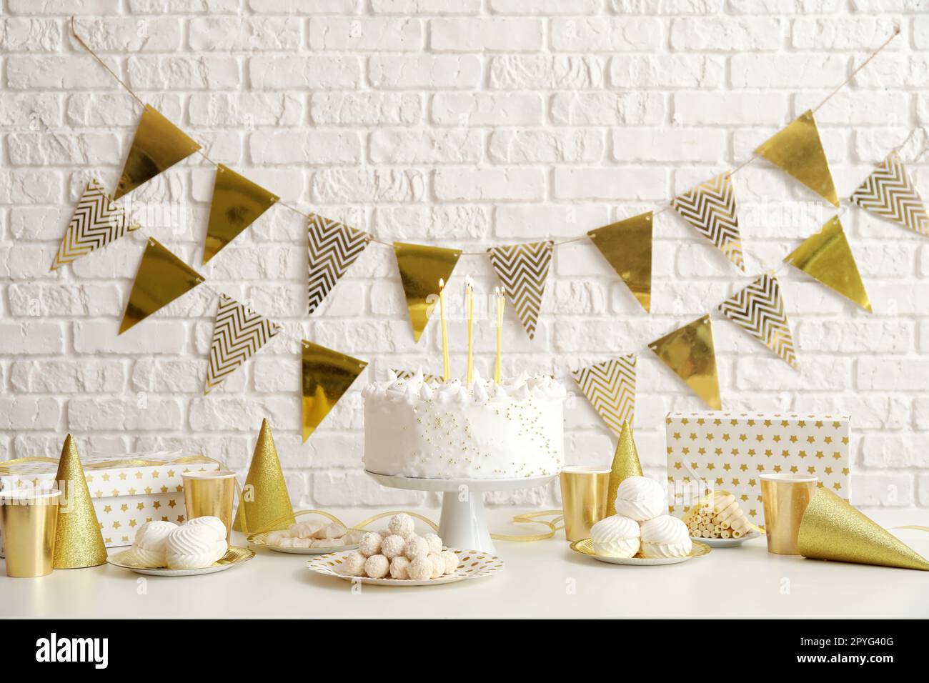 Birthday cake with candles and sweets on white table near brick wall ...