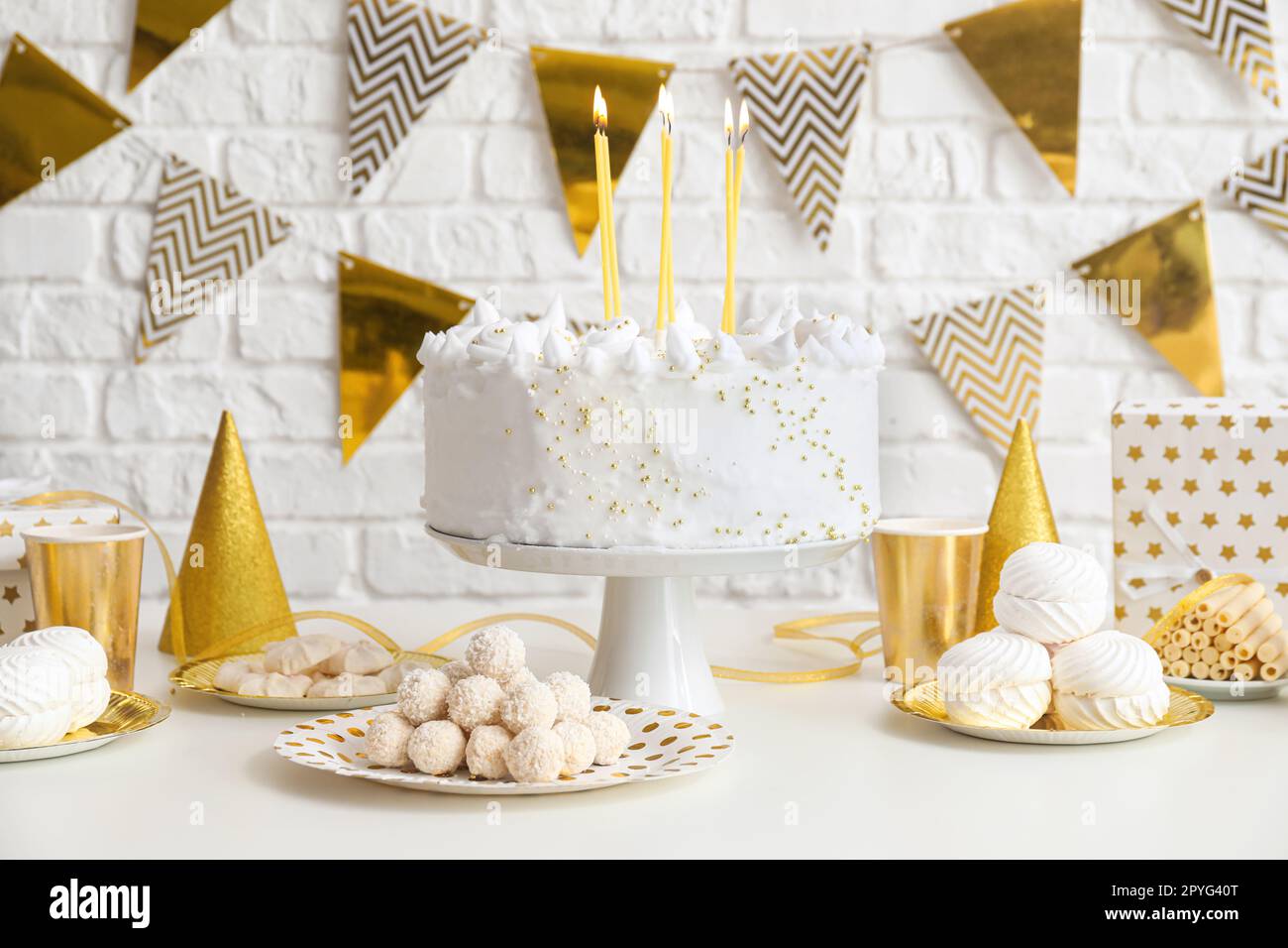 Birthday cake with candles and sweets on white table near brick wall ...