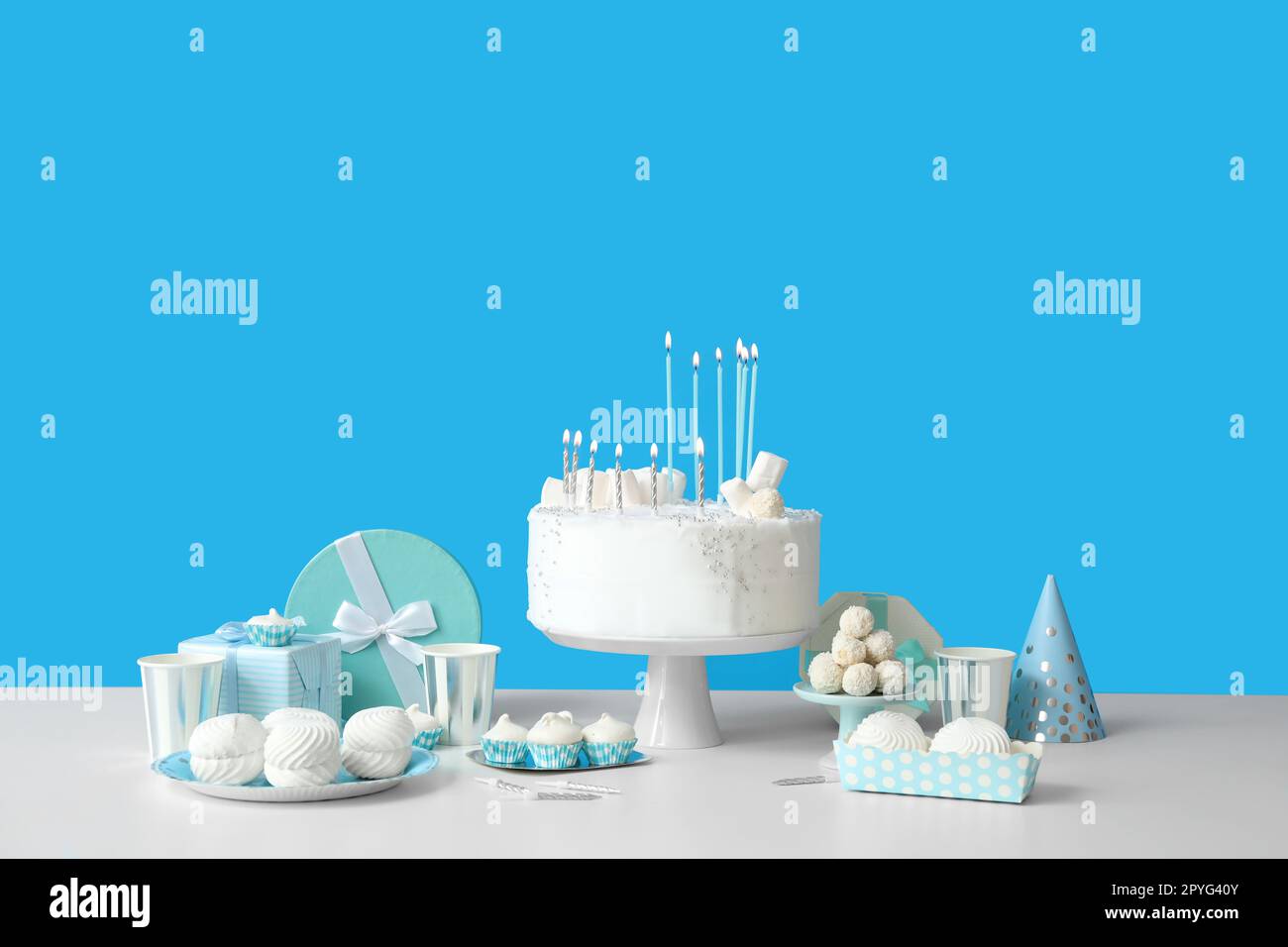 Birthday cake with candles and sweets on white table near blue wall ...