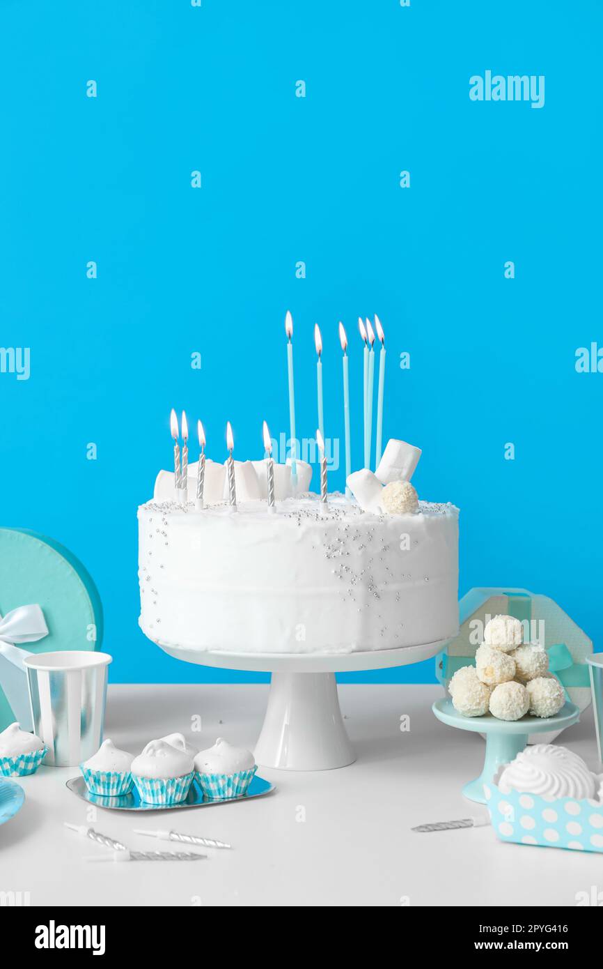 Birthday cake with candles and sweets on white table near blue wall ...