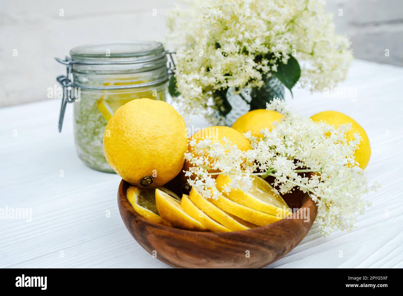 Slices of fresh lemon in a wooden plate. Ingredients for herbal tea from elder syrup. Snappy ambucus stalks ready to make a cold summer drink Stock Photo