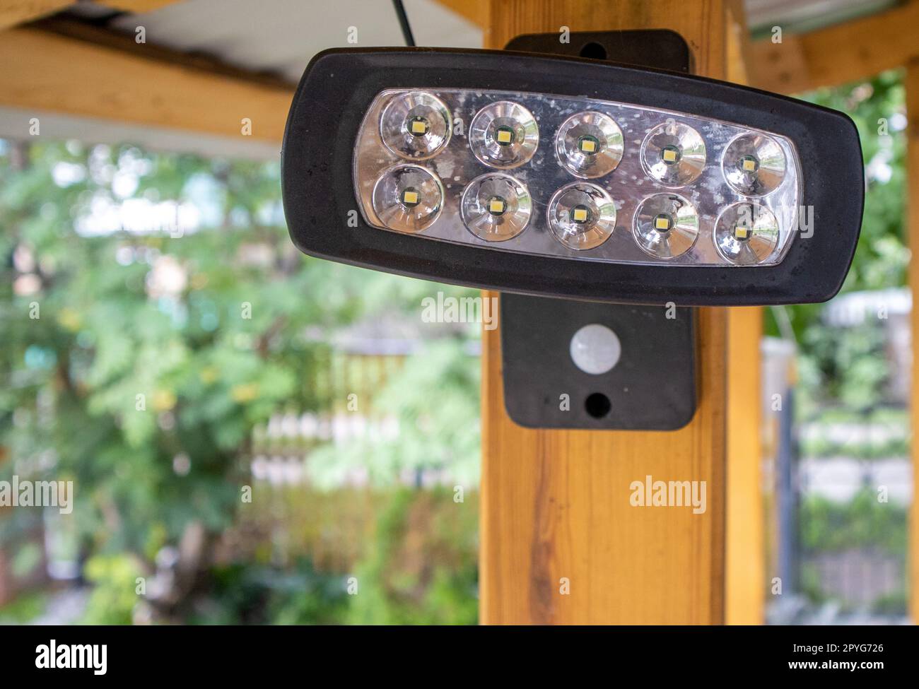 Close-up of an LED spotlight, a spotlight on a wooden post of an open veranda, on a blurred background of the garden. A lantern for lighting the house territory at night Stock Photo