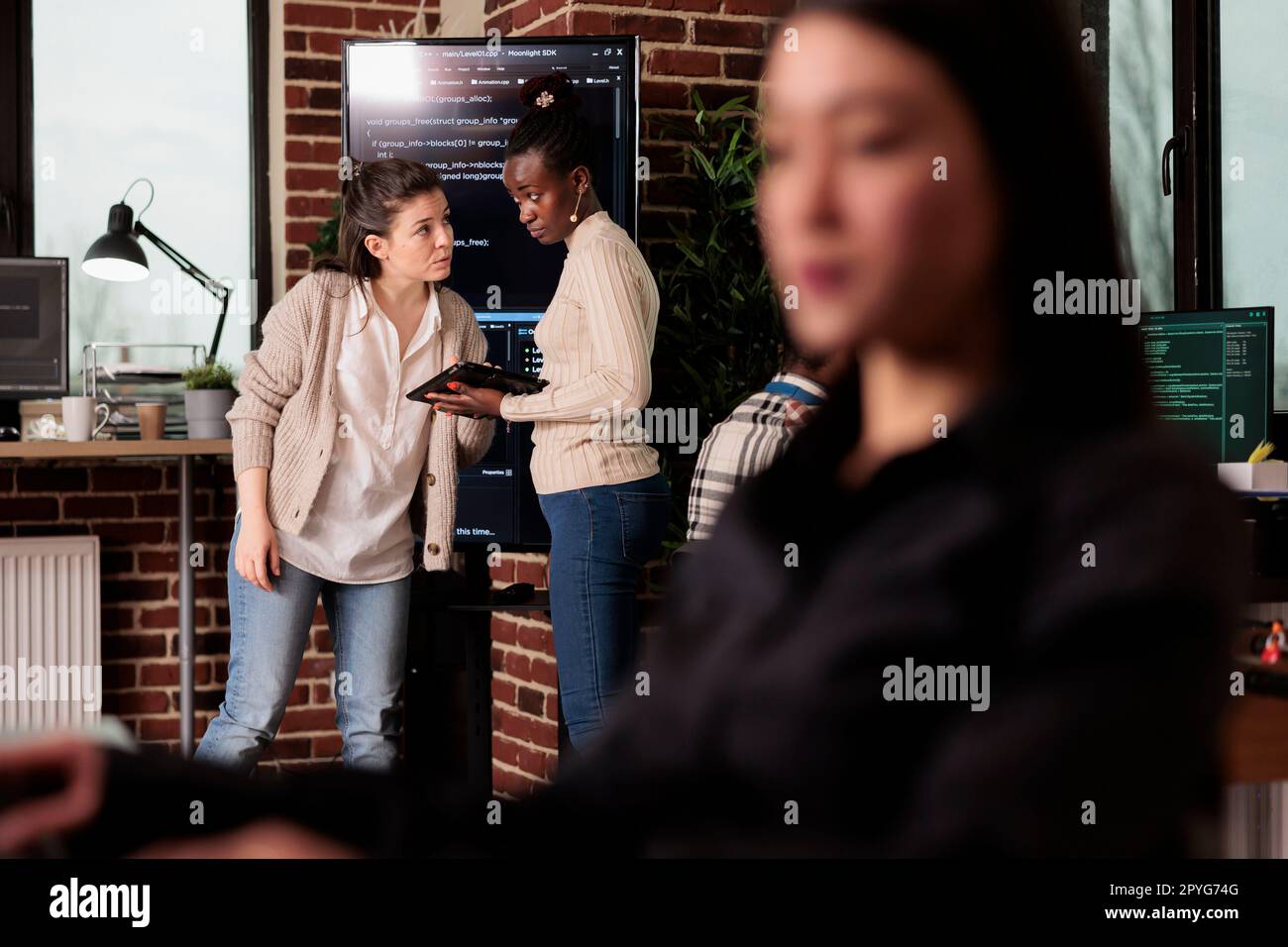 Two software developers analyzing source code looking for errors, checking big tv monitor in it agency office. Tech enginners working on cyber security innovation in it programming agency. Stock Photo