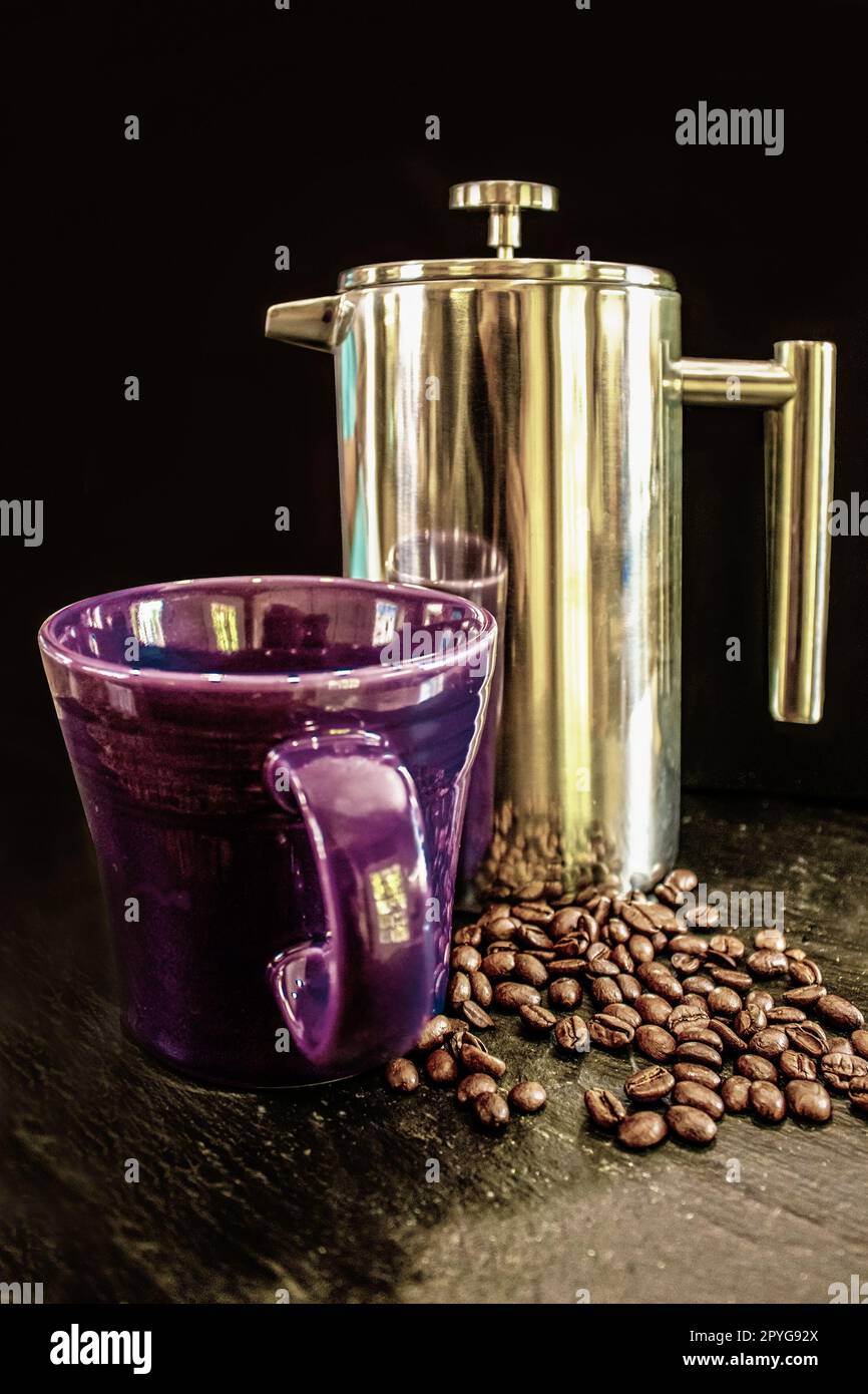 Purple cup and chrome French press and coffee beans against black background sitting of rough slate surface Stock Photo