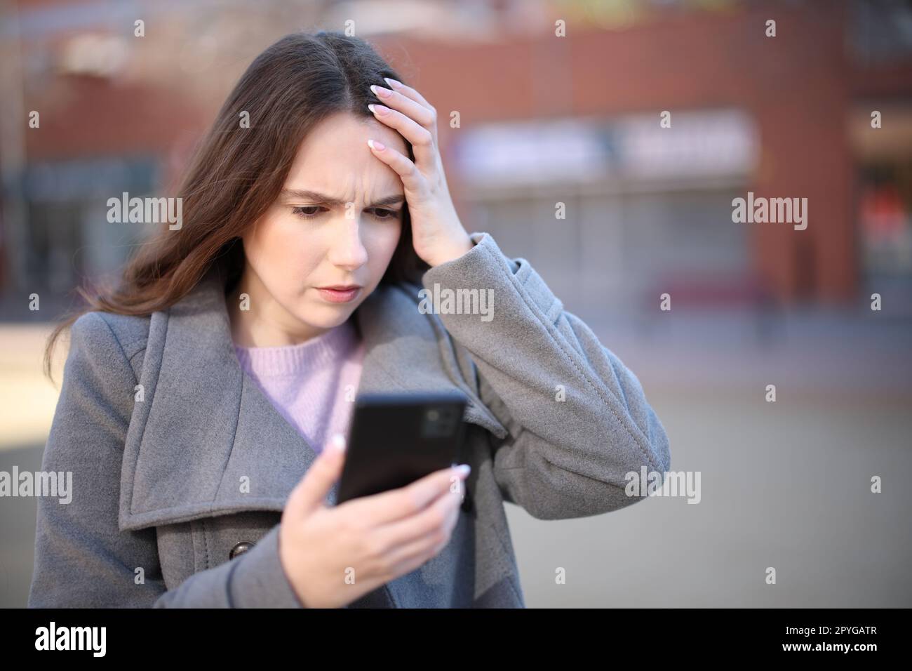 Worried woman checking smart phone in winter Stock Photo